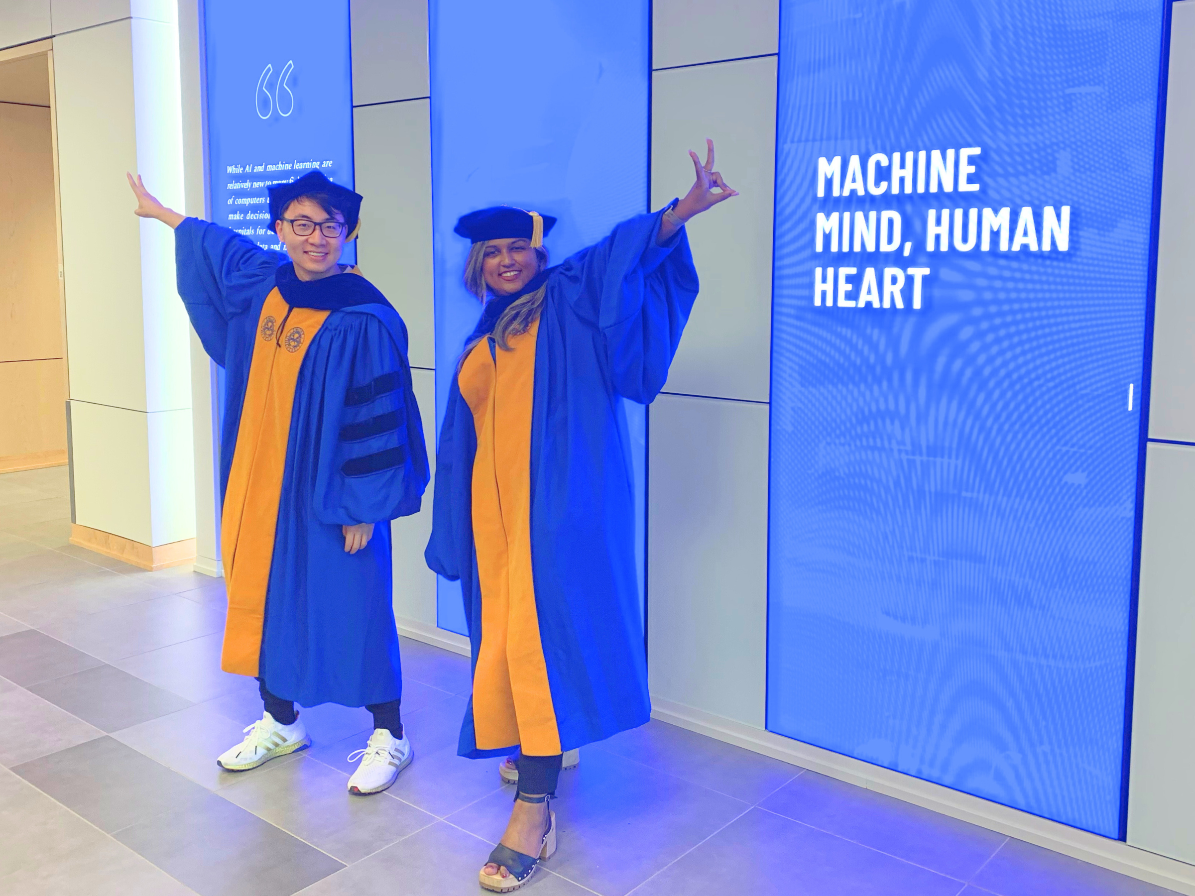 Class of 2023 PhD graduates Yuxin Duan and Aysha Rashid pose in front of Wonder Wall in HSRB I
