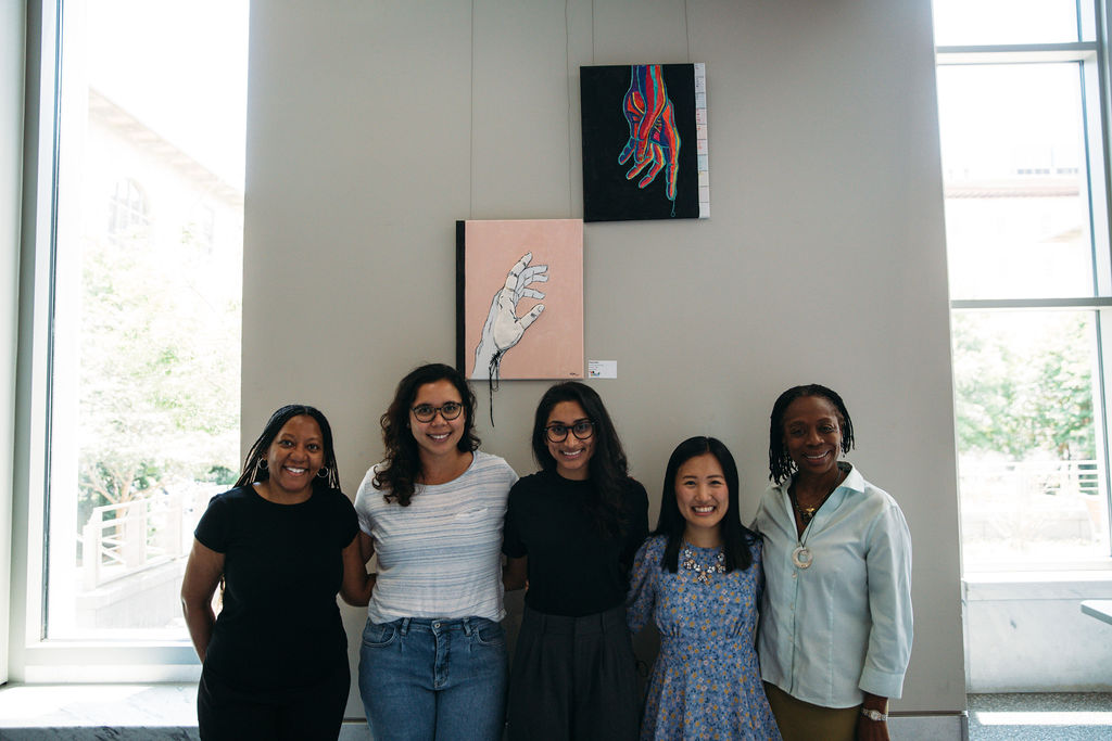 5 women standing in front of two paintings hung on a wall