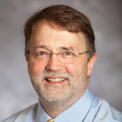 a headshot of a man wearing a yellow tie and glasses smiling at the camera