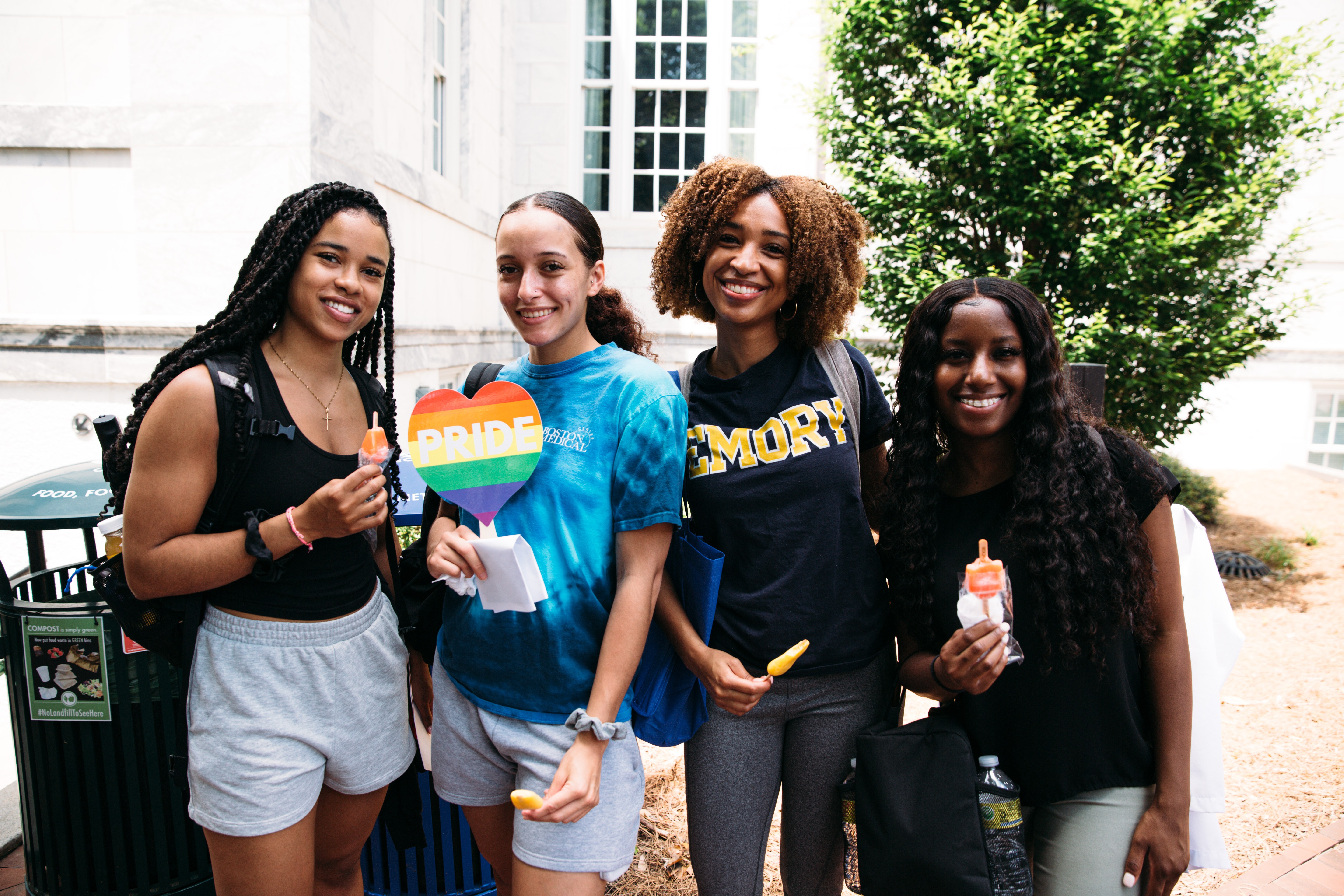 Four women stand in a row eating popsicles and smiling