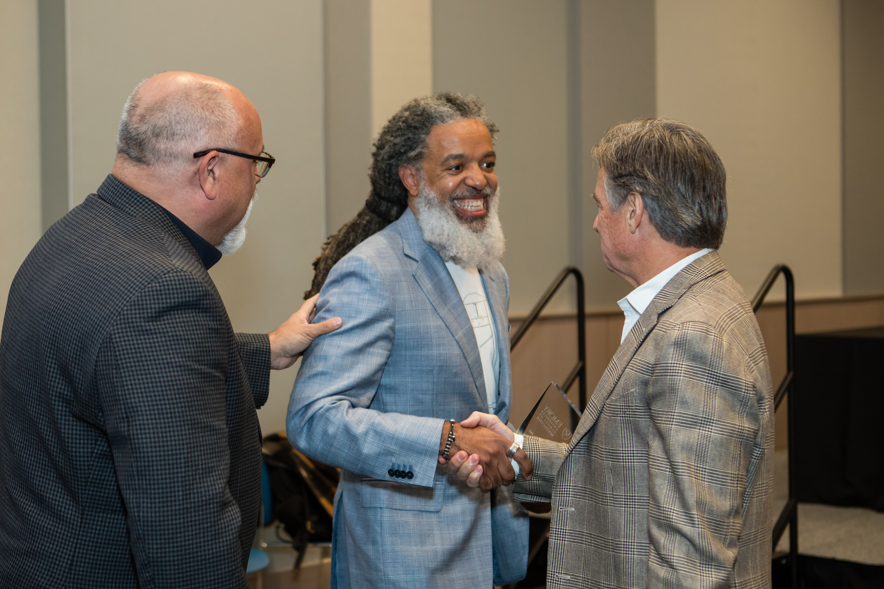 Three men stand together with one man shaking the other man's hand.