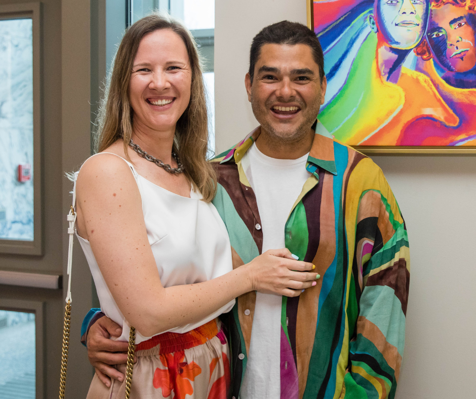 A man and a woman stand in front of art work smiling.