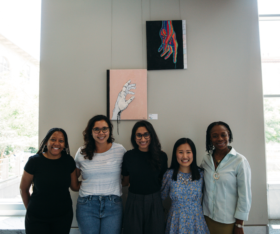 Group of women stand in front of painting of hands