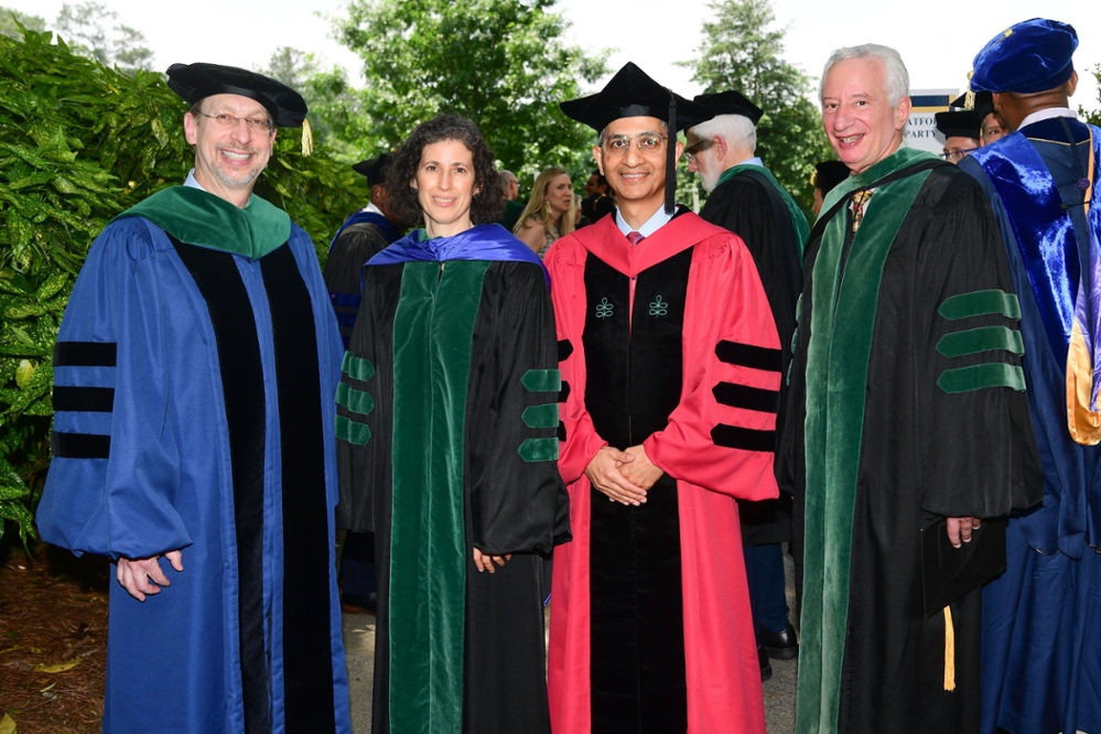 Dean and three Associate Deans posing in graduation ceremony robes