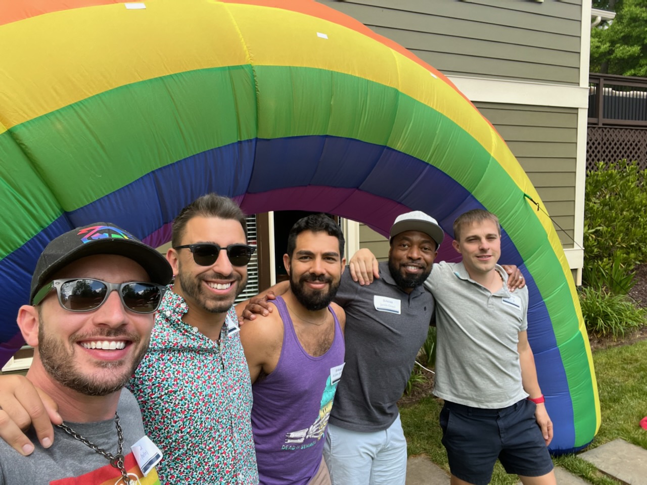 Five men smile for a photo in front of an inflatable rainbow.
