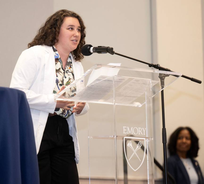A young woman with dark curly hair standing at a podium speaking