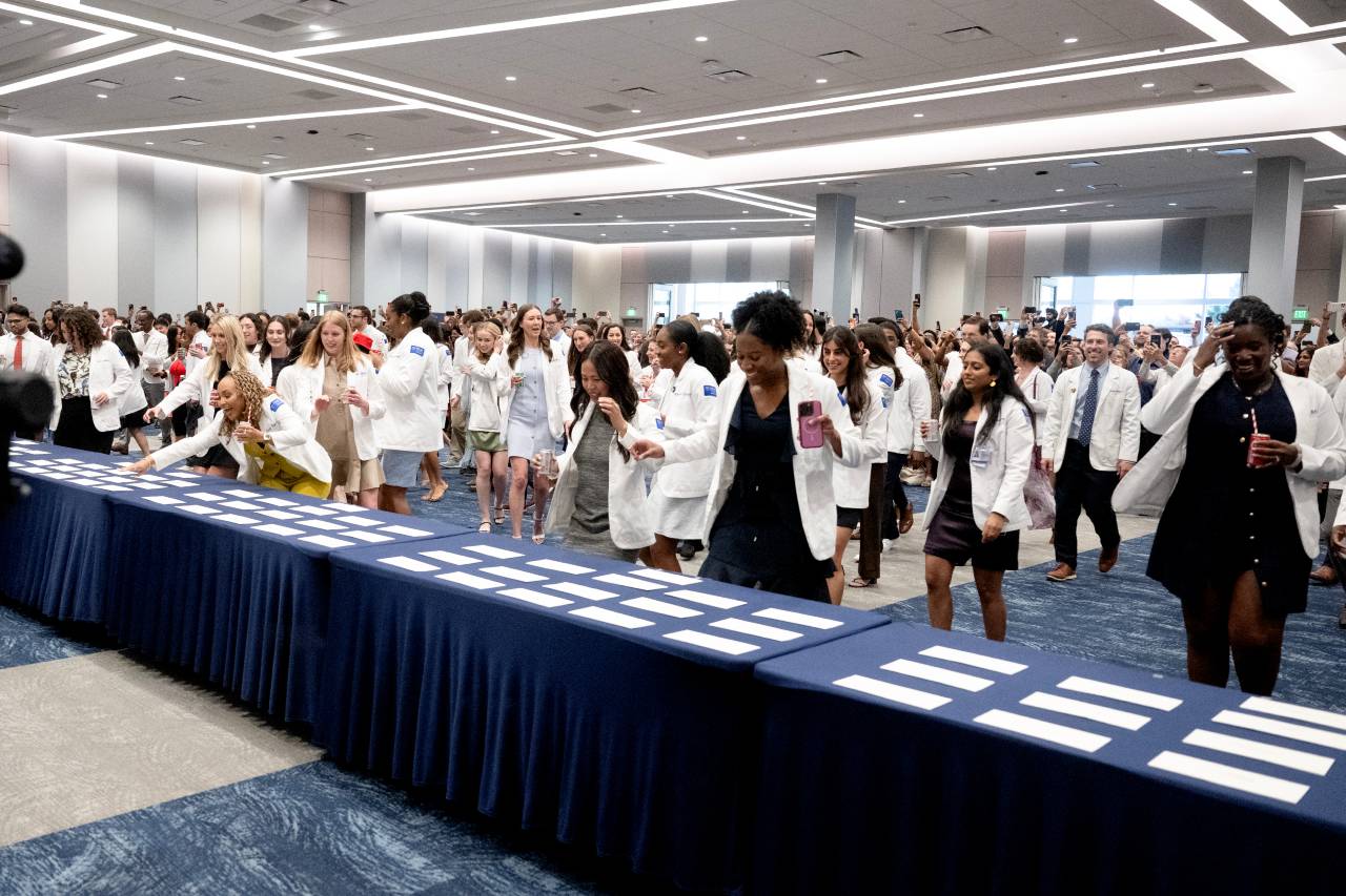 large group in white coats running towards a blue table with white envelopes