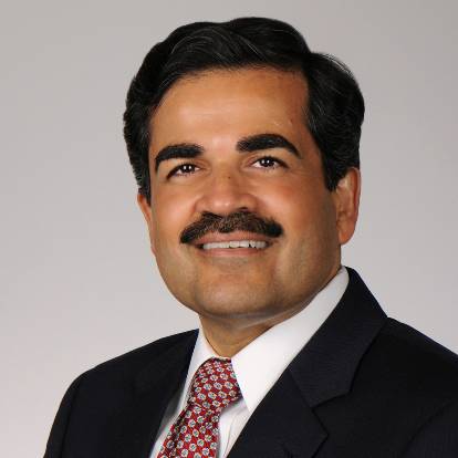 headshot of a man in a dark suit, red, patterned tie and a mustache