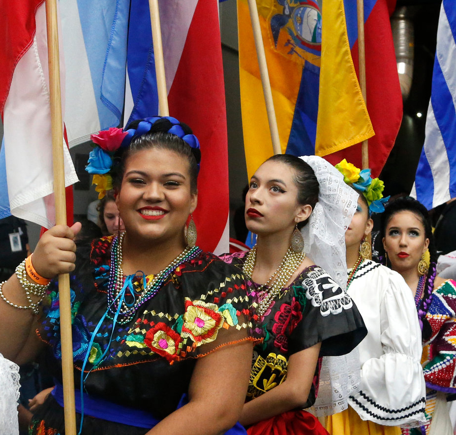 Women wear traditional outfits and hold their countries flag at a Hispanic Heritage Month event