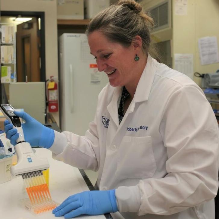 Anne Roberts sitting at lab bench with pipette