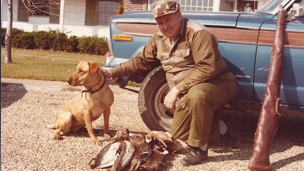 man dressed in hunting clothes petting dog