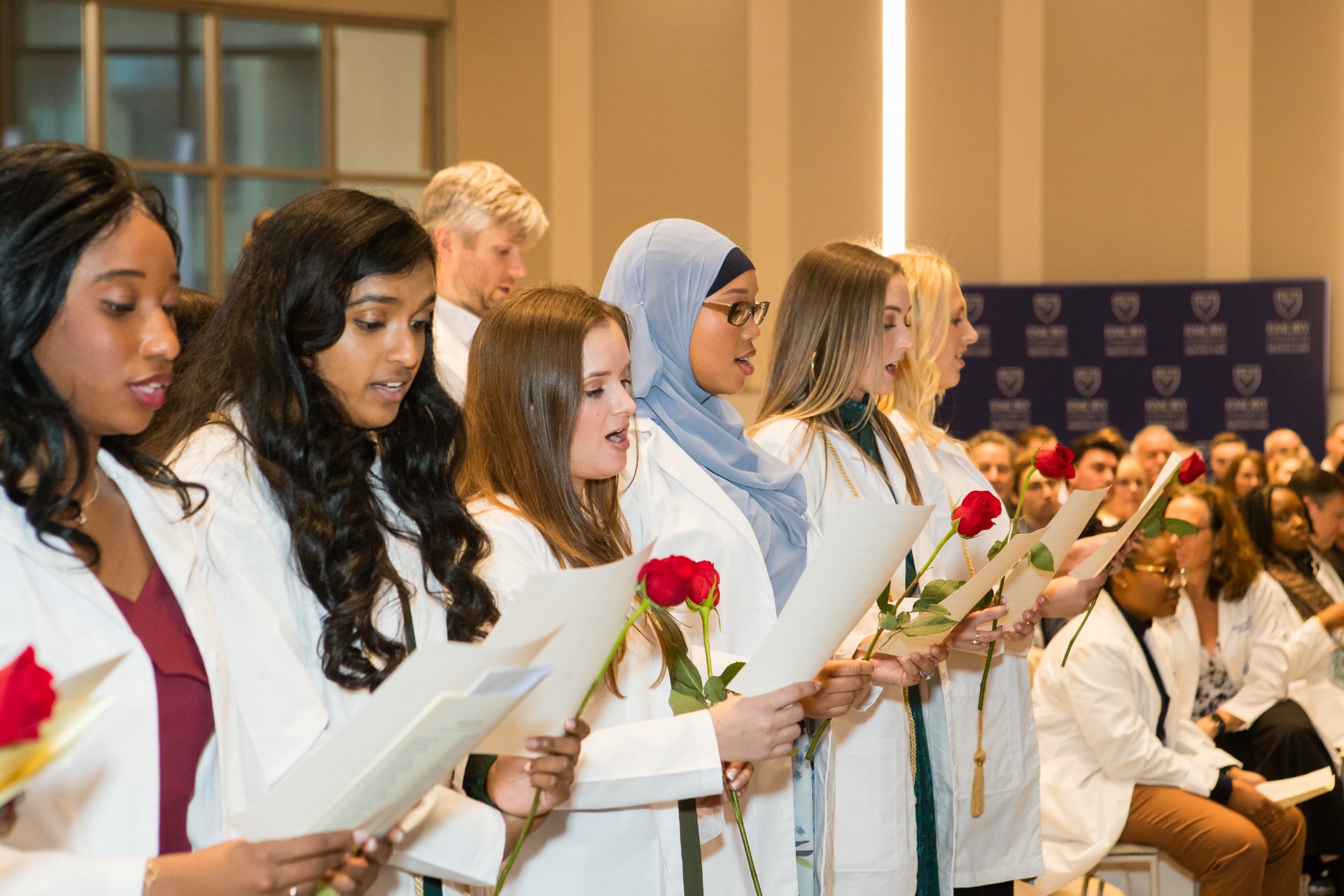 a group of PA students reciting the PA Oath. The women students are holding red roses and a sheet of paper with the oath printed on it