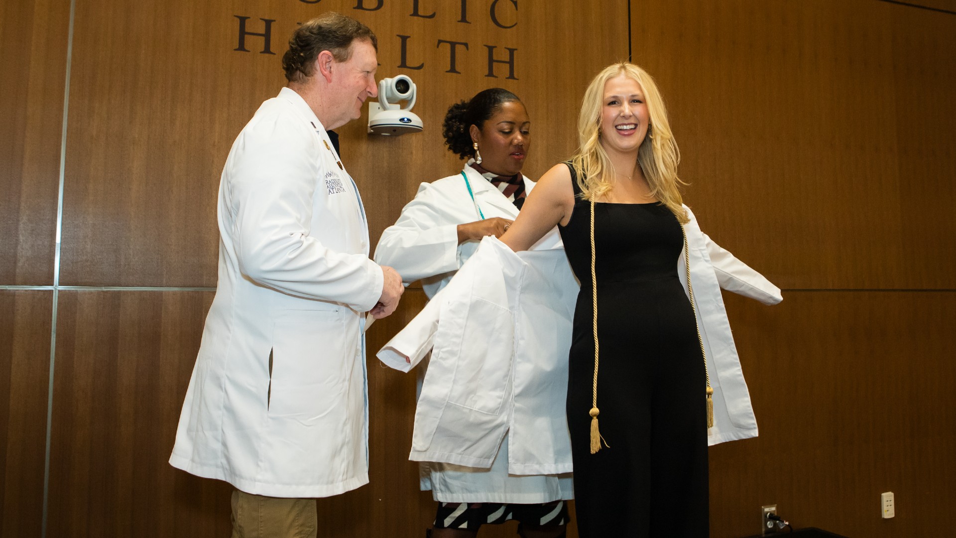 two faculty members assisting a PA student who is putting on her white coat