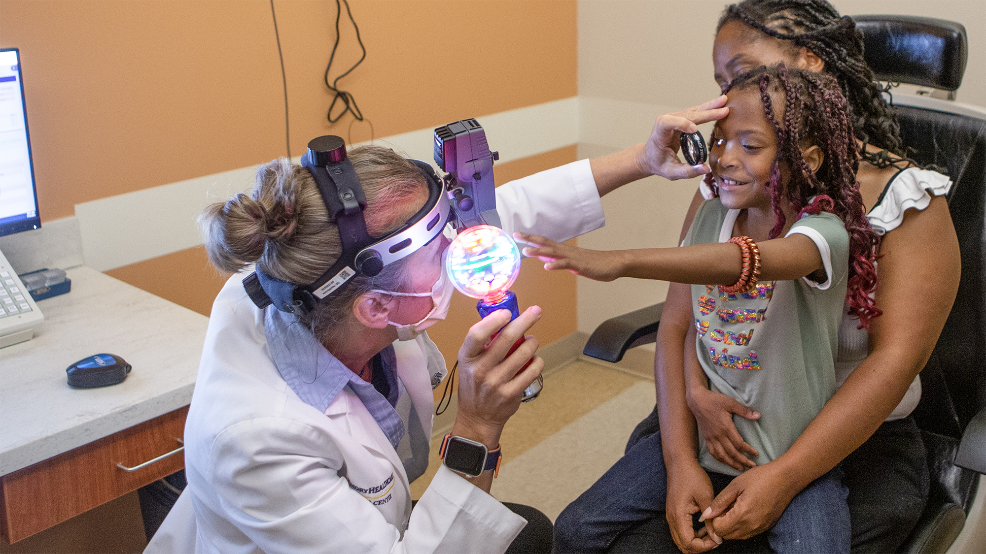 Dr. Amy Hutchinson performing a vision test on a young girl who is sitting in her mother's lap