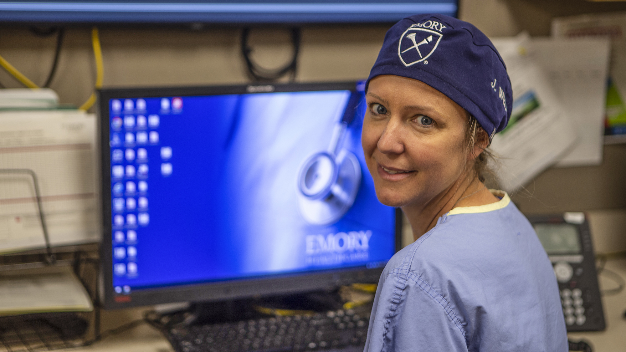 Dr. Jill Wells, in scrubs, sitting in front of a computer after performing surgery