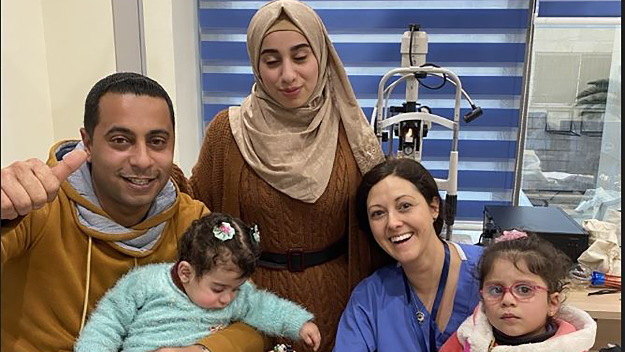 A Jordanian mother and father with their toddler and infant pose in an exam room with a GO-E clinician
