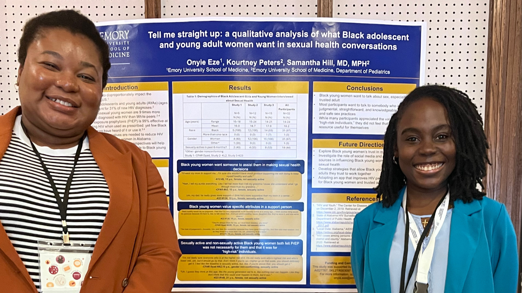 Two people in front of a Tell Me Straight Up presentation poster.