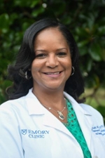 smiling person wearing a white medical coat over a green top