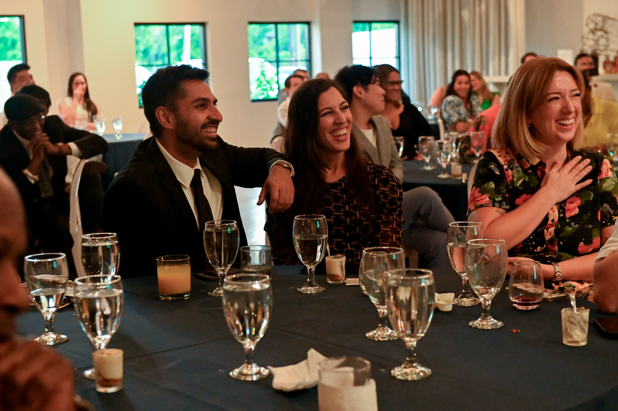 people seated at a round table with other people in the background at a party