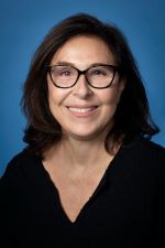 smiling woman with shoulder length brown hair wearing dark rimmed spectacles and a black v-neck shirt