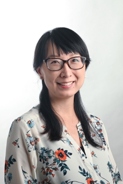 smiling womanwith black bangs across forehead and straight down shoulders wearing dark rimmed glasses and a colorful floral top