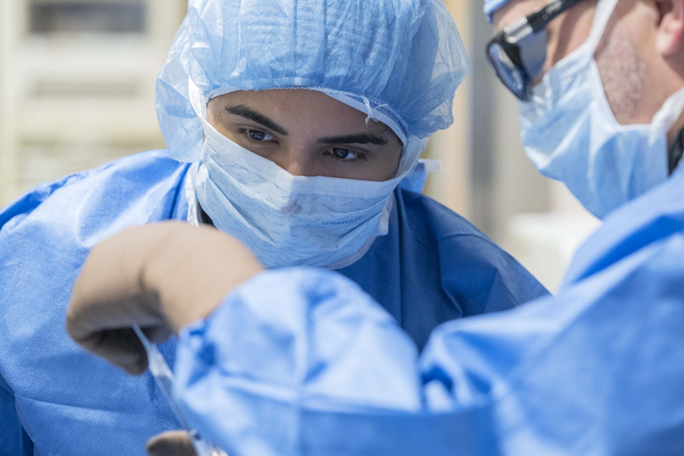 female trainee is shown how to perform an image-guided procedure by male IR faculty member both wearing blue scrubes and white face masks covering their noses and mouths