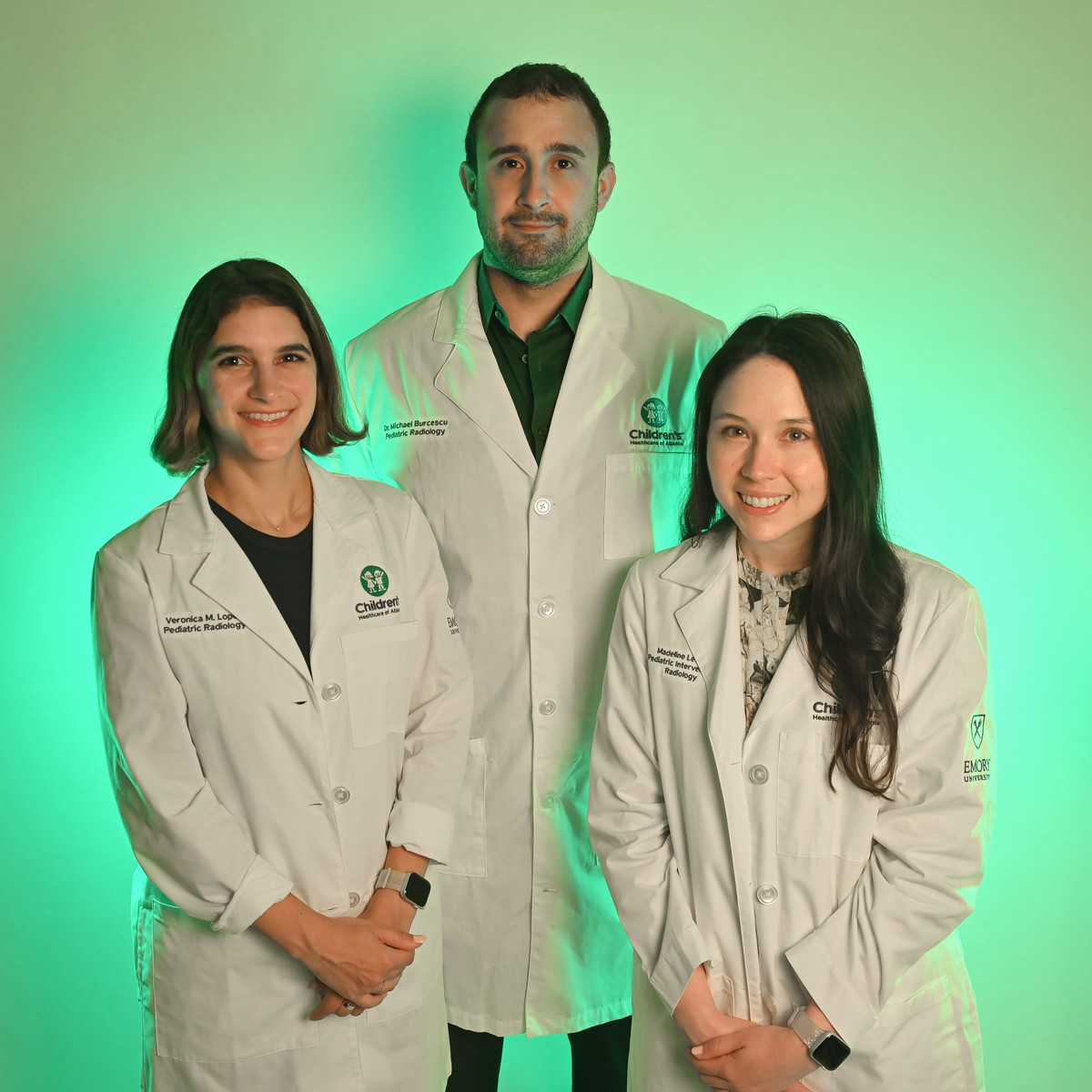 three people wearing white doctor coats over business clothes standing together with a green background