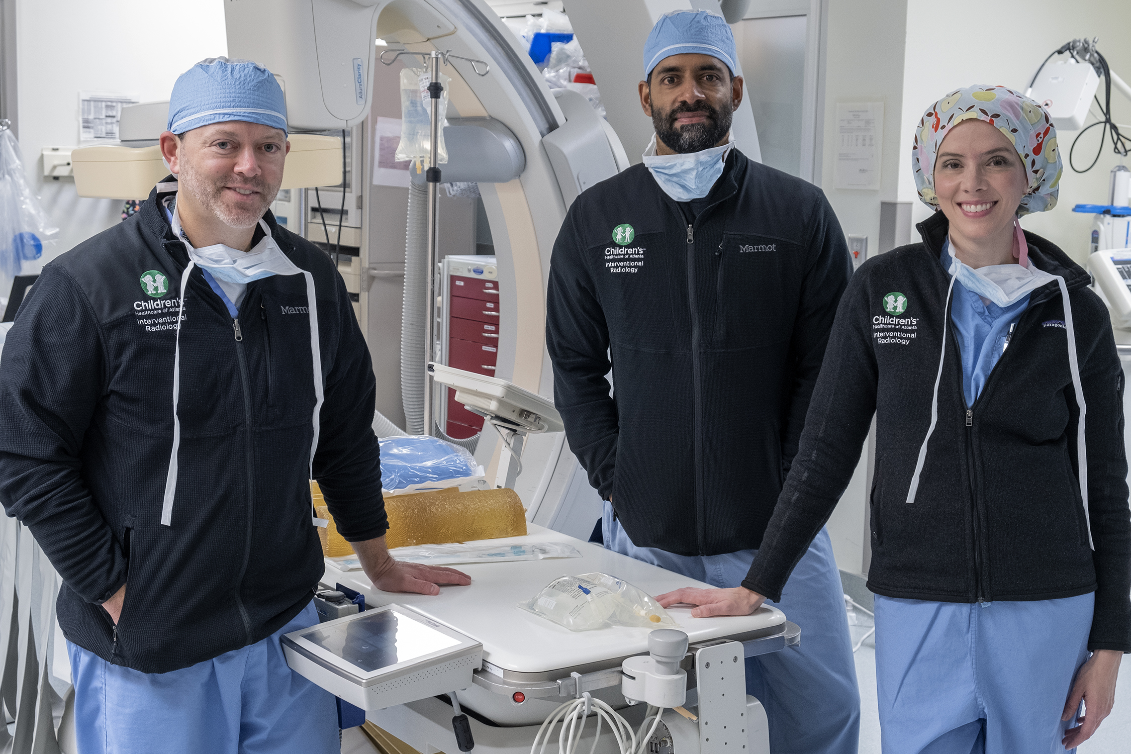 two male and one female pediatric interventional radiologists smiling and wearing blue scrubs