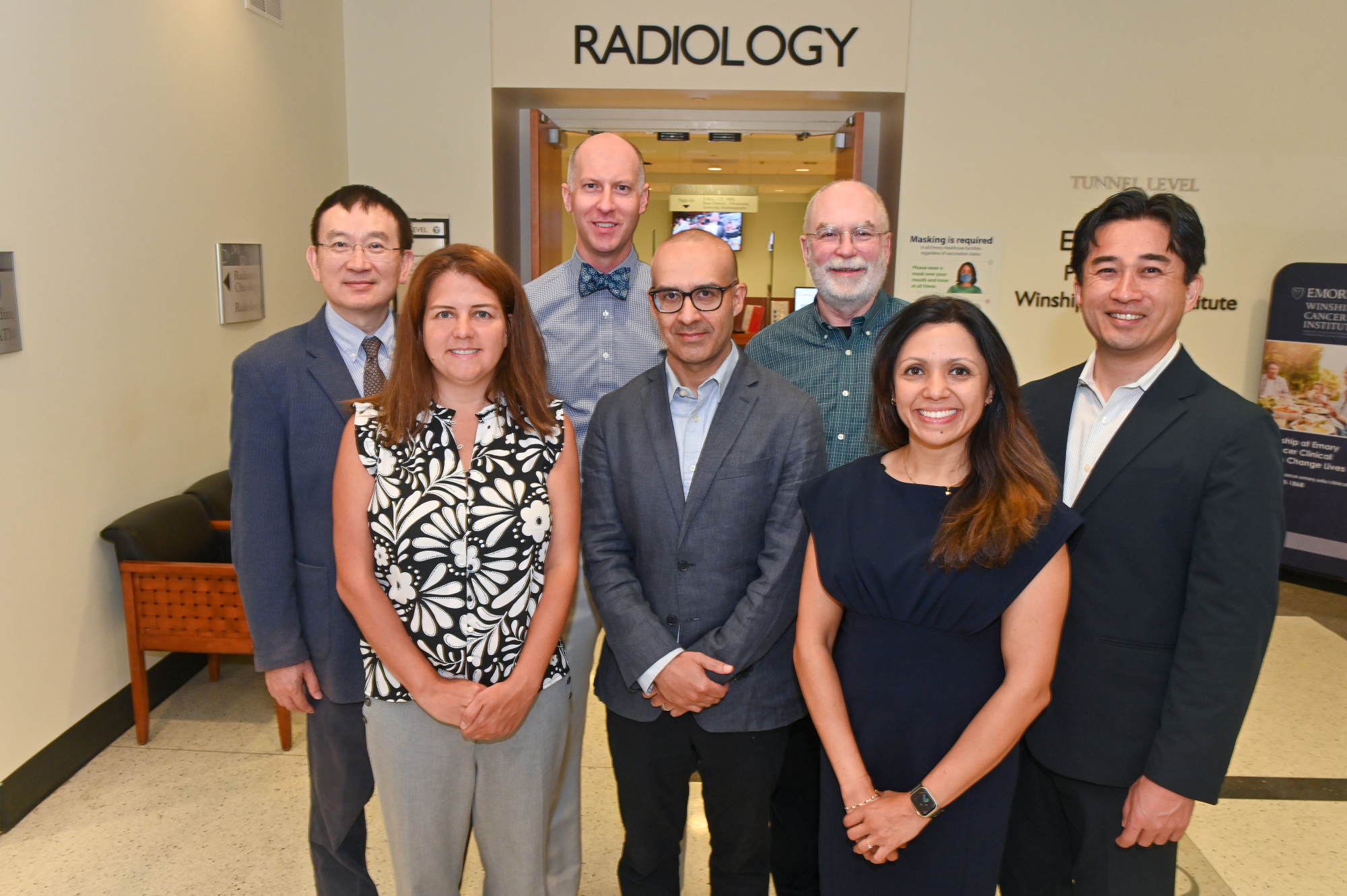 seven people standing in a hallway together with the words Radiology on the wall behind them