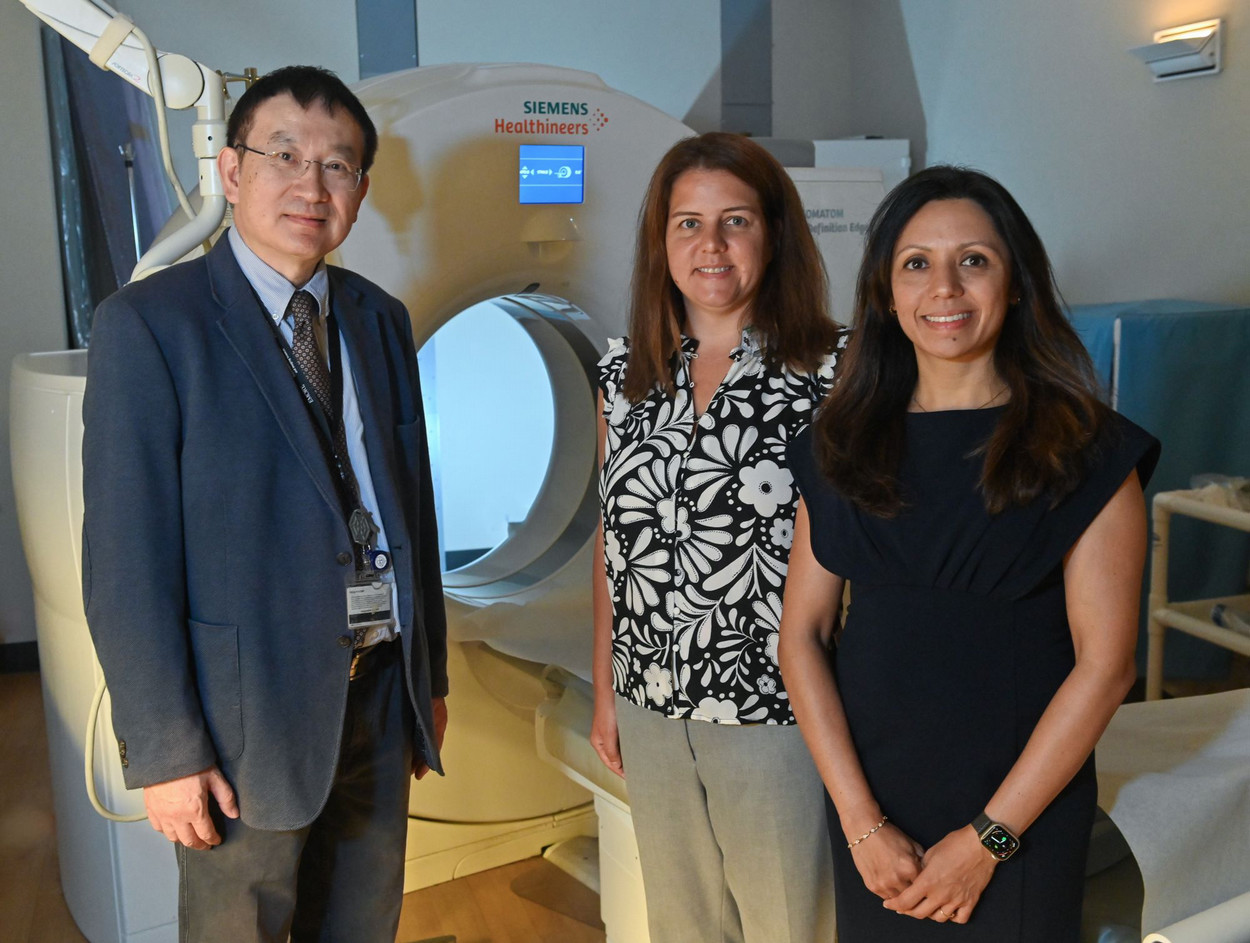 three people standing beside a CT imaging machine in a room with low light