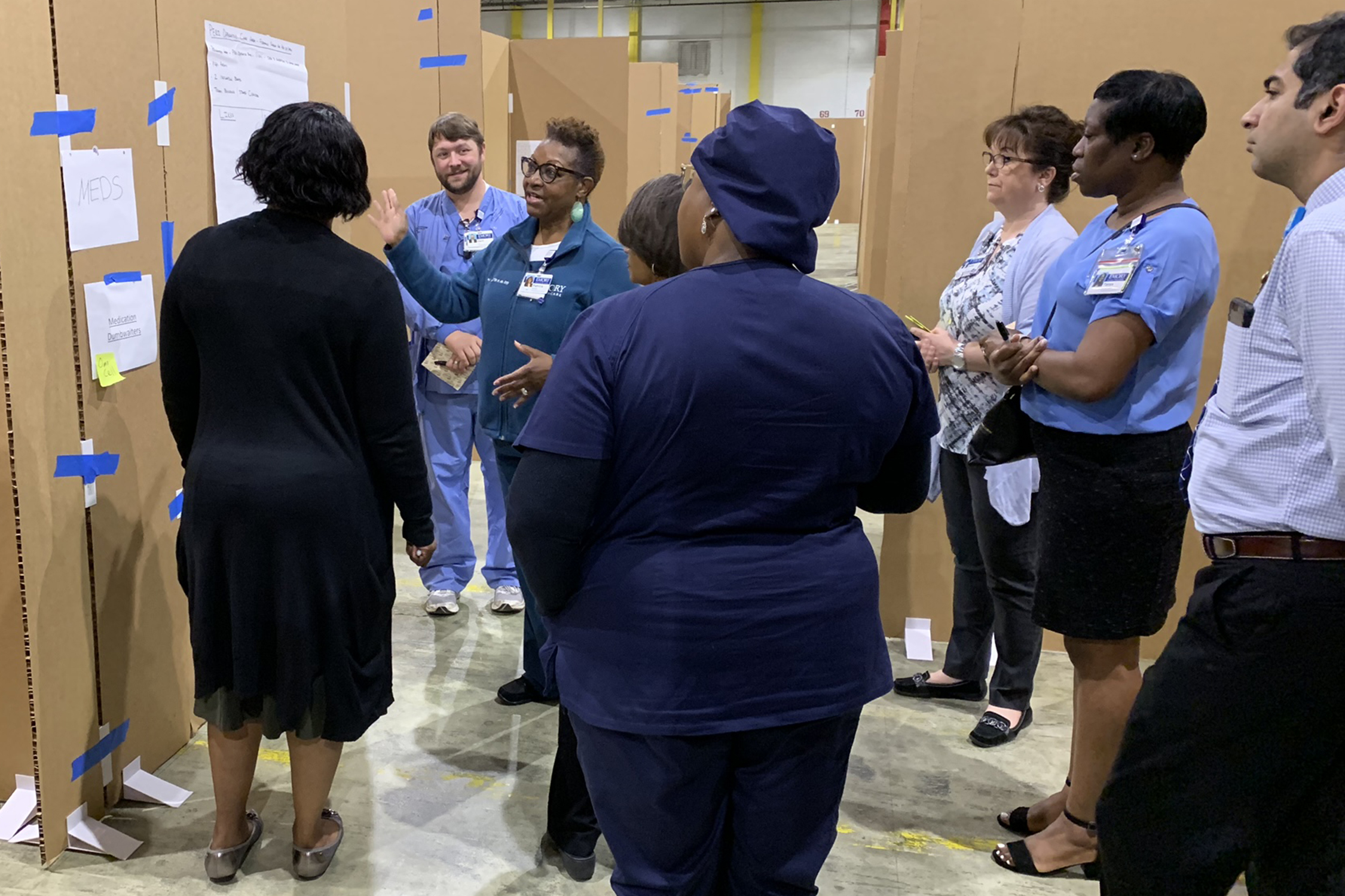 people standing around cardboard version of an office listening to a speaker