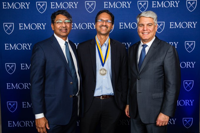 three men smiling in front of Emory branded step and repeat