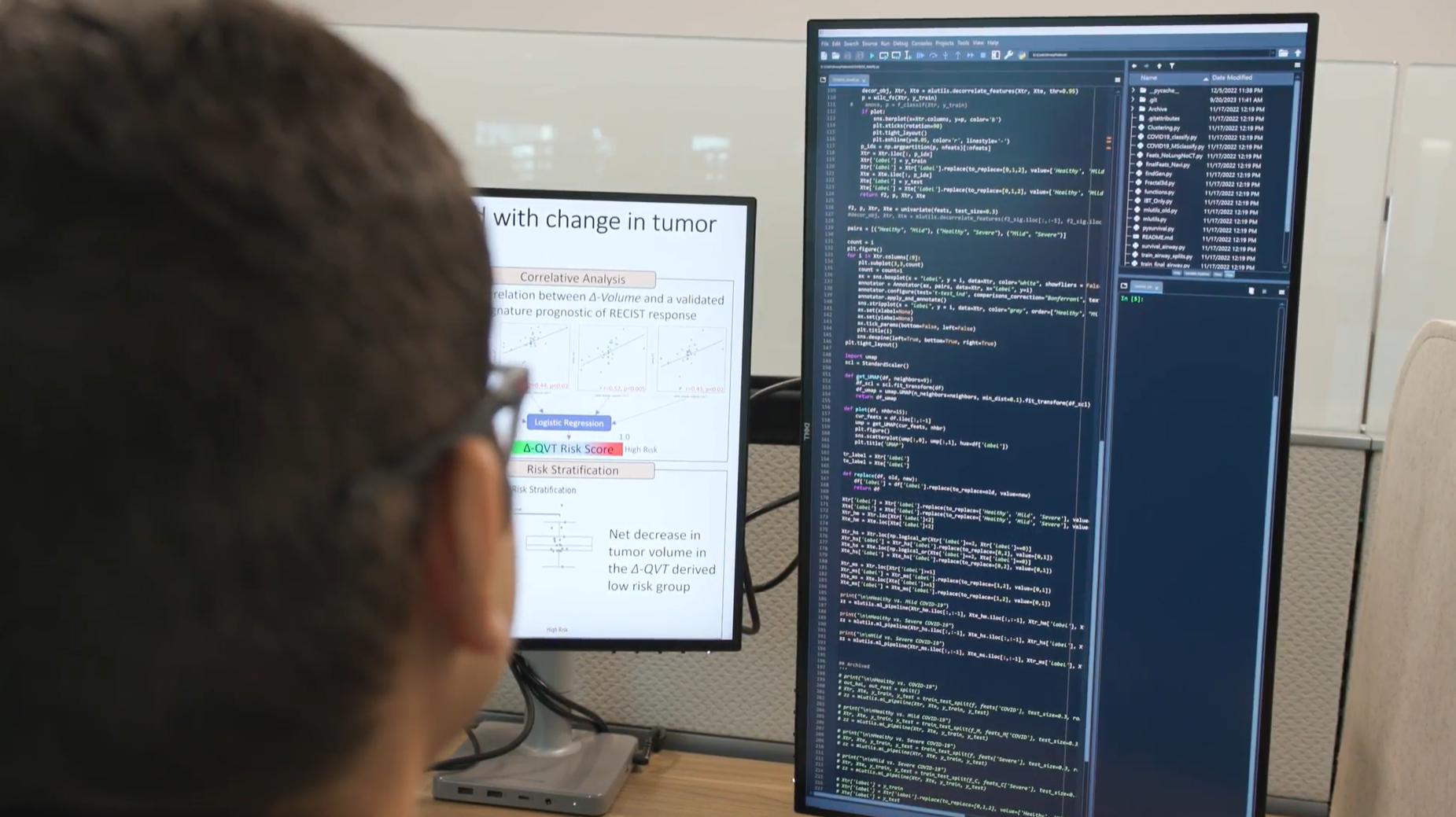 person seated at a computer workstation looking at data regarding tumors on the right side vertical monitor and text with illustrative images on the other monitor