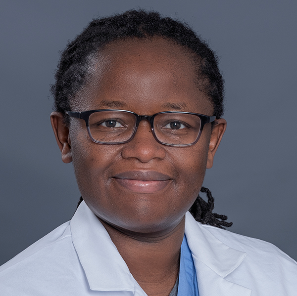 smiling woman with black hair pulled back from face into small braids at neck wearing white doctor coat and light blue scrubs and dark square eyeglasses
