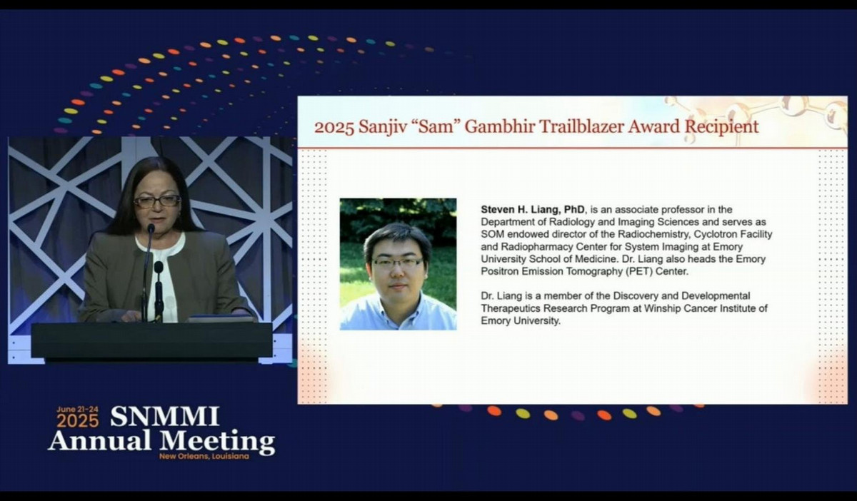 scientist standing at podium at SNMMI Annual Meeting with slide showing Steven Liang projected beside them