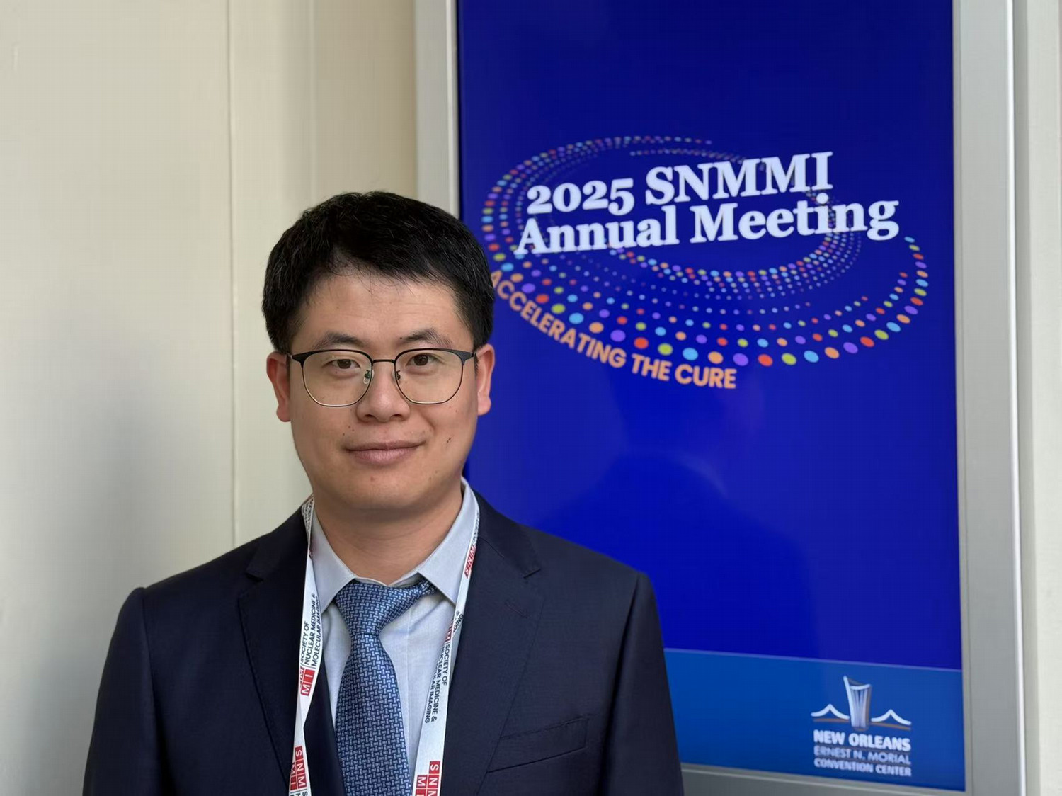 scientist smiling in front of 2025 SNMMI Annual Meeting banner