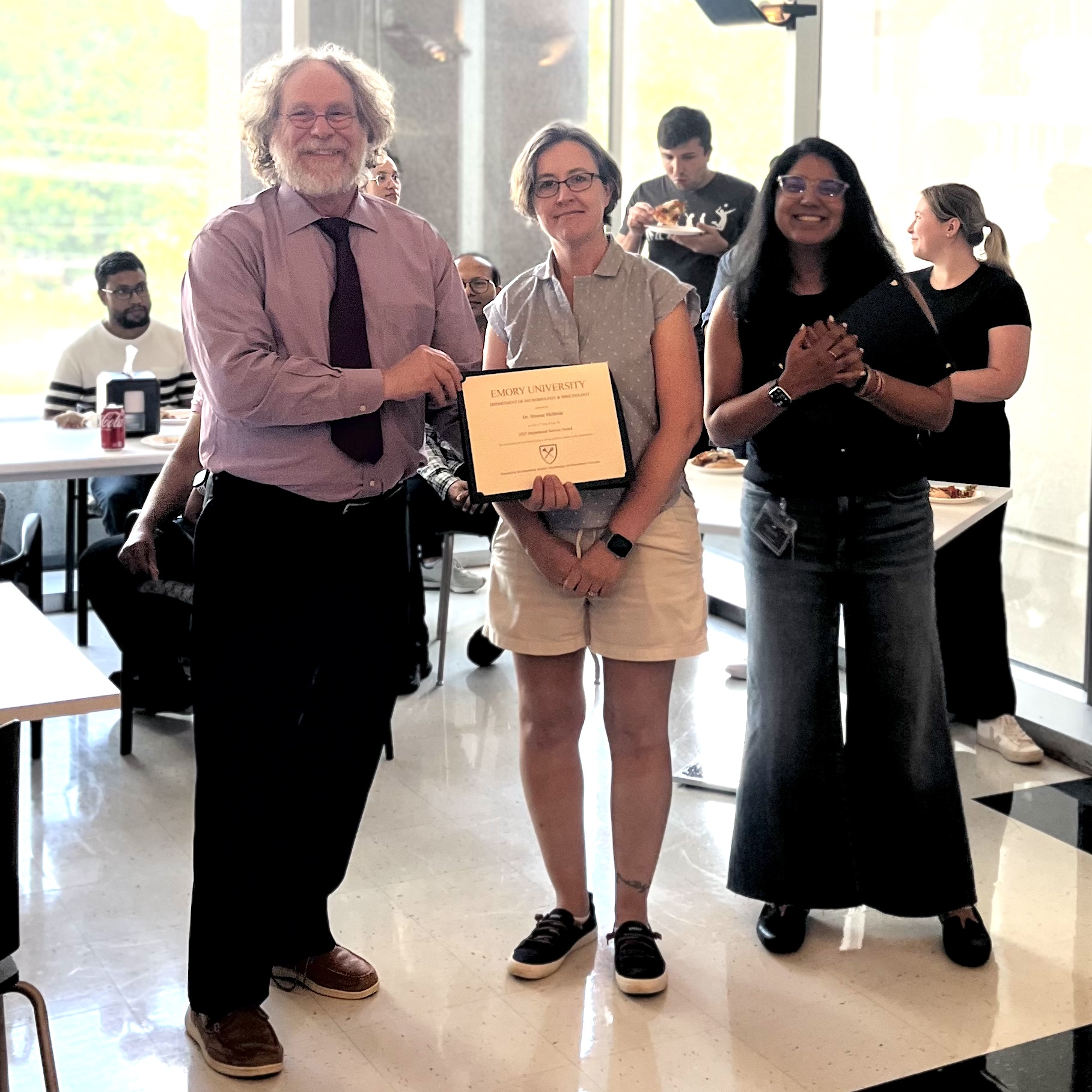 one man, two women, standing at award ceremony, one person holding a certificate