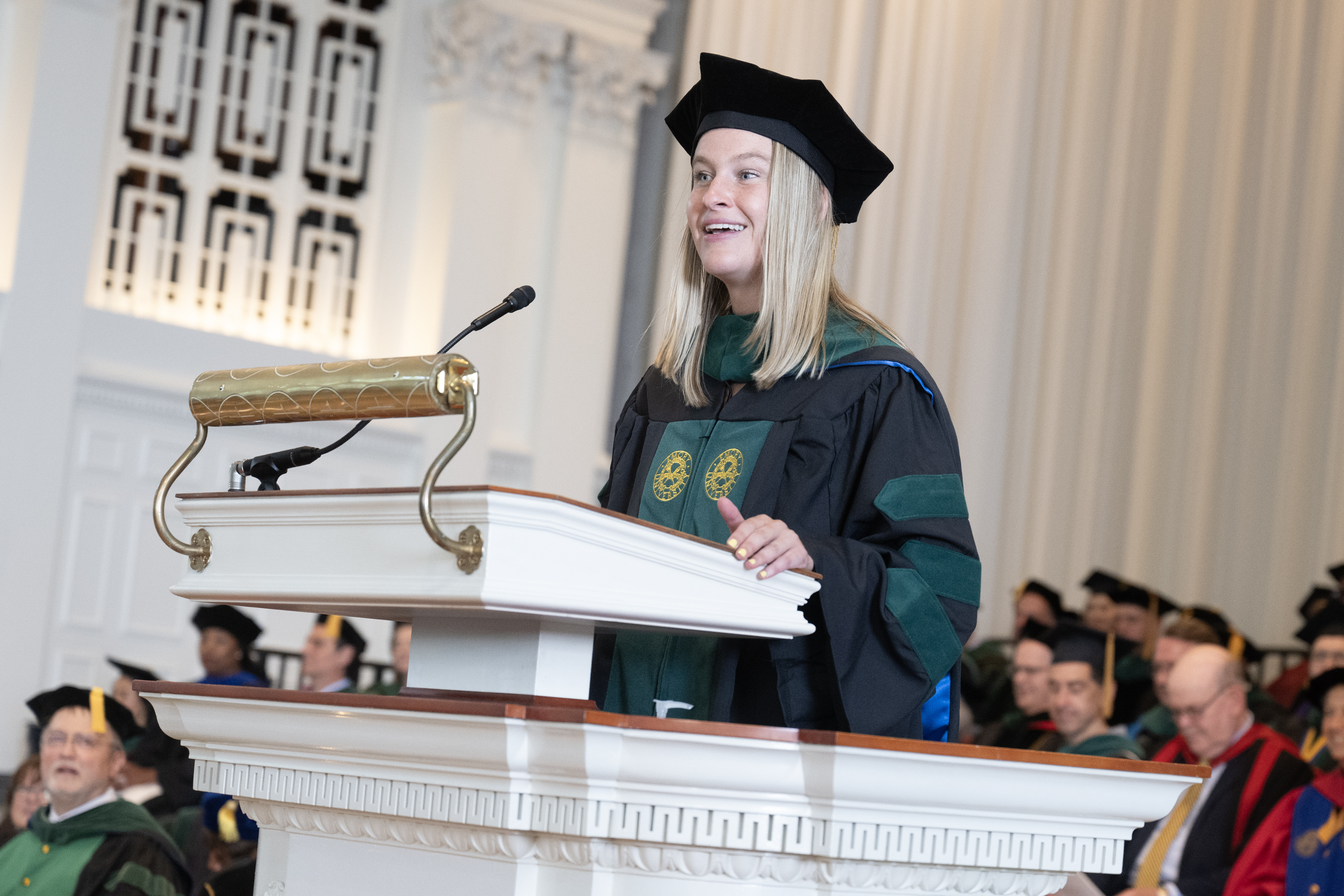 Class President Maeve McNamara addresses graduating class at podium.