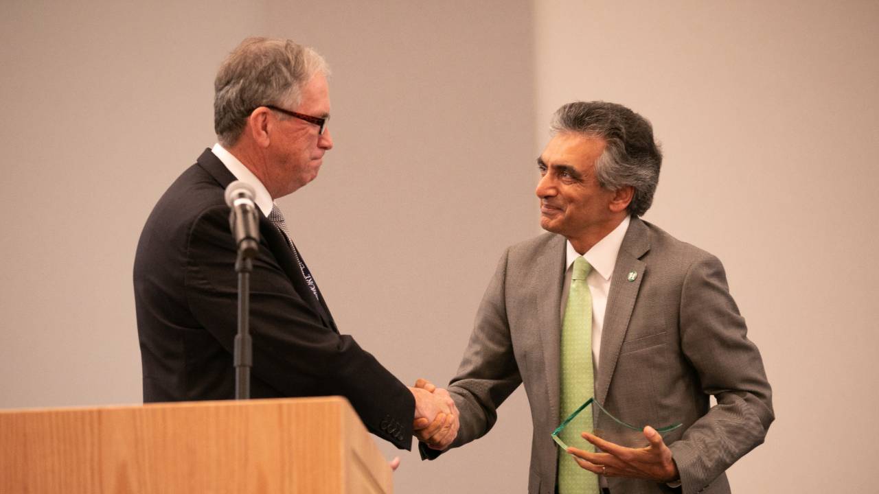 Two men shaking hands one holding a glass award