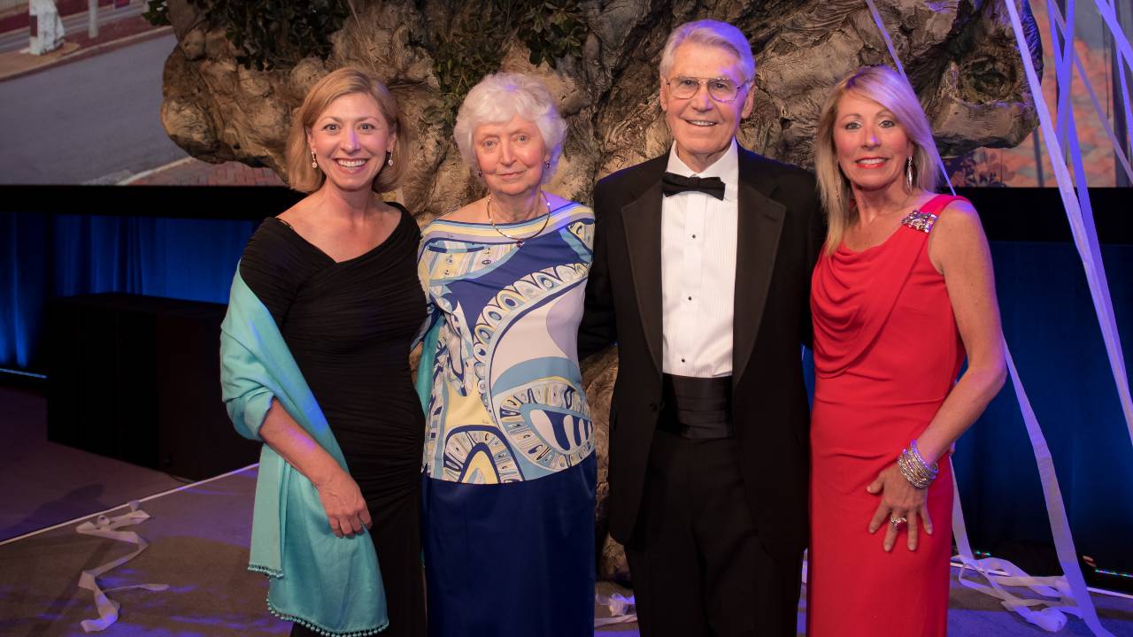 Four people standing in a row dressed formally