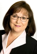 smiling person wearing spectacles and a dark suit jacket over a white blouse open at the collar