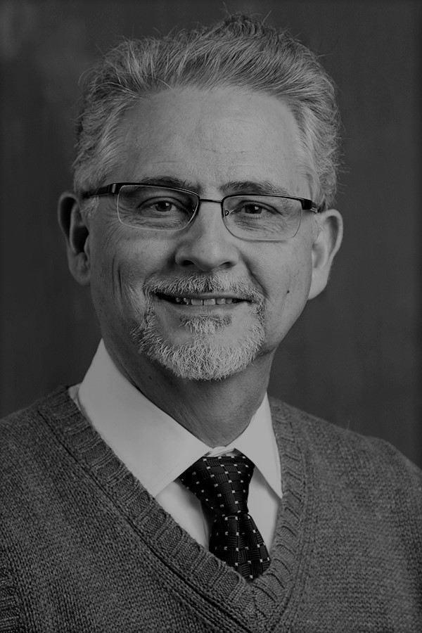 smiling person with goatee and short silvery hair wearing spectacles and a sweater over a dress shirt and tie