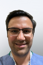 headshot of doctor wearing blue scrubs top, spectacles