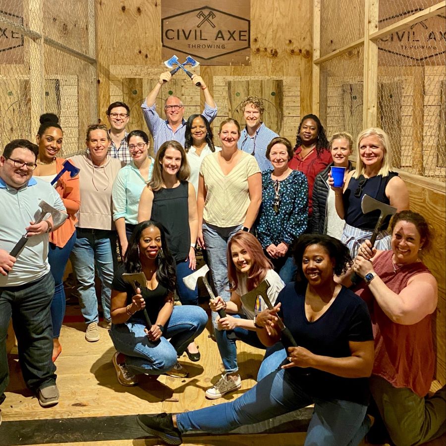 people smiling in a group of standing and seated people some of whom are holding axes in front of sign that says civil axe throwing