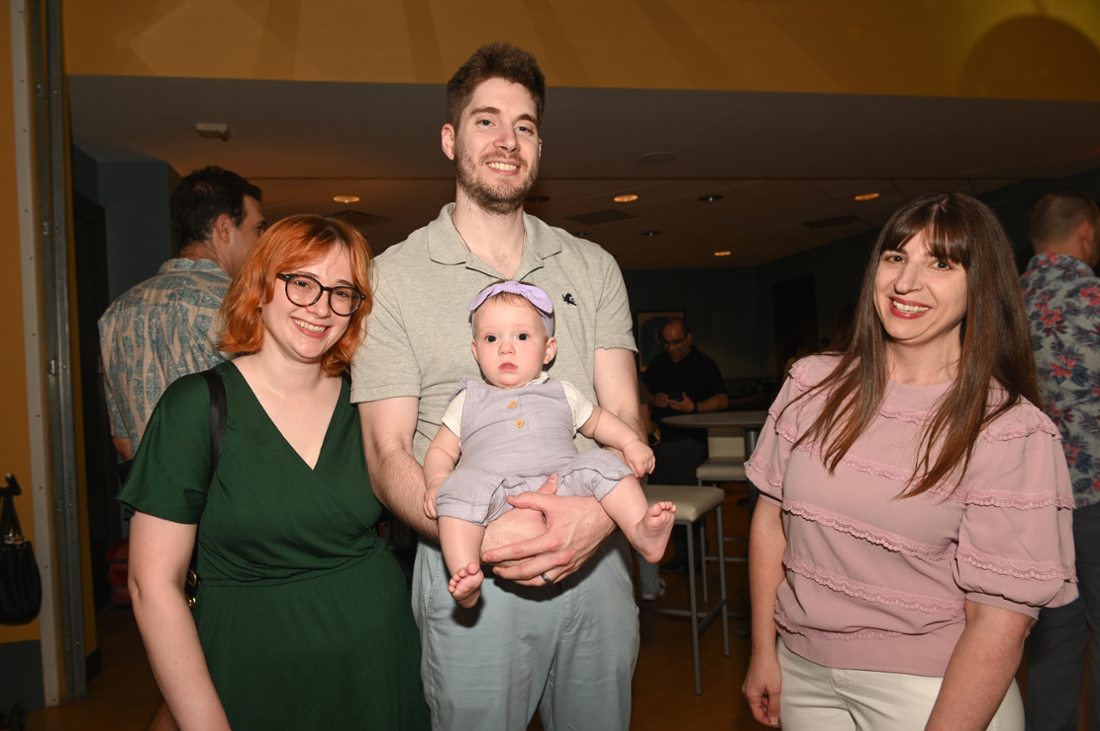 person holding baby smiling and standing between two other people who are smiling