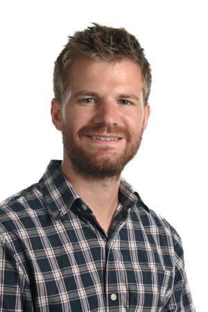 smiling person with reddish moustache and beard and short hair wearing a blue and white checked shirt