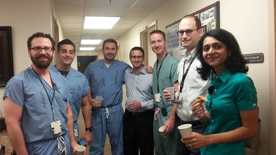 seven people standing in a semicircle in a hospital hallway smiling at the camera