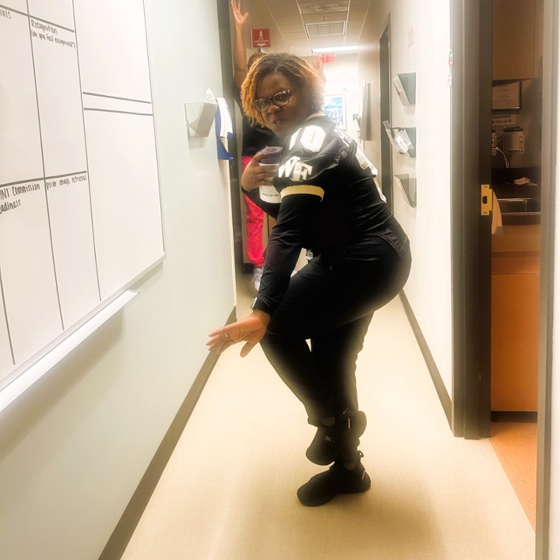 person with fierce expression wearing football jersey strikes a pose like a football player defending possession of a ball while standing in a hallway