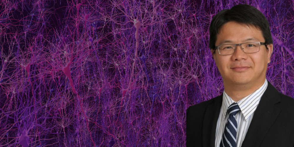 smiling person in dark suit with dark striped tie is in front of images of neuronal networks in shades of purple