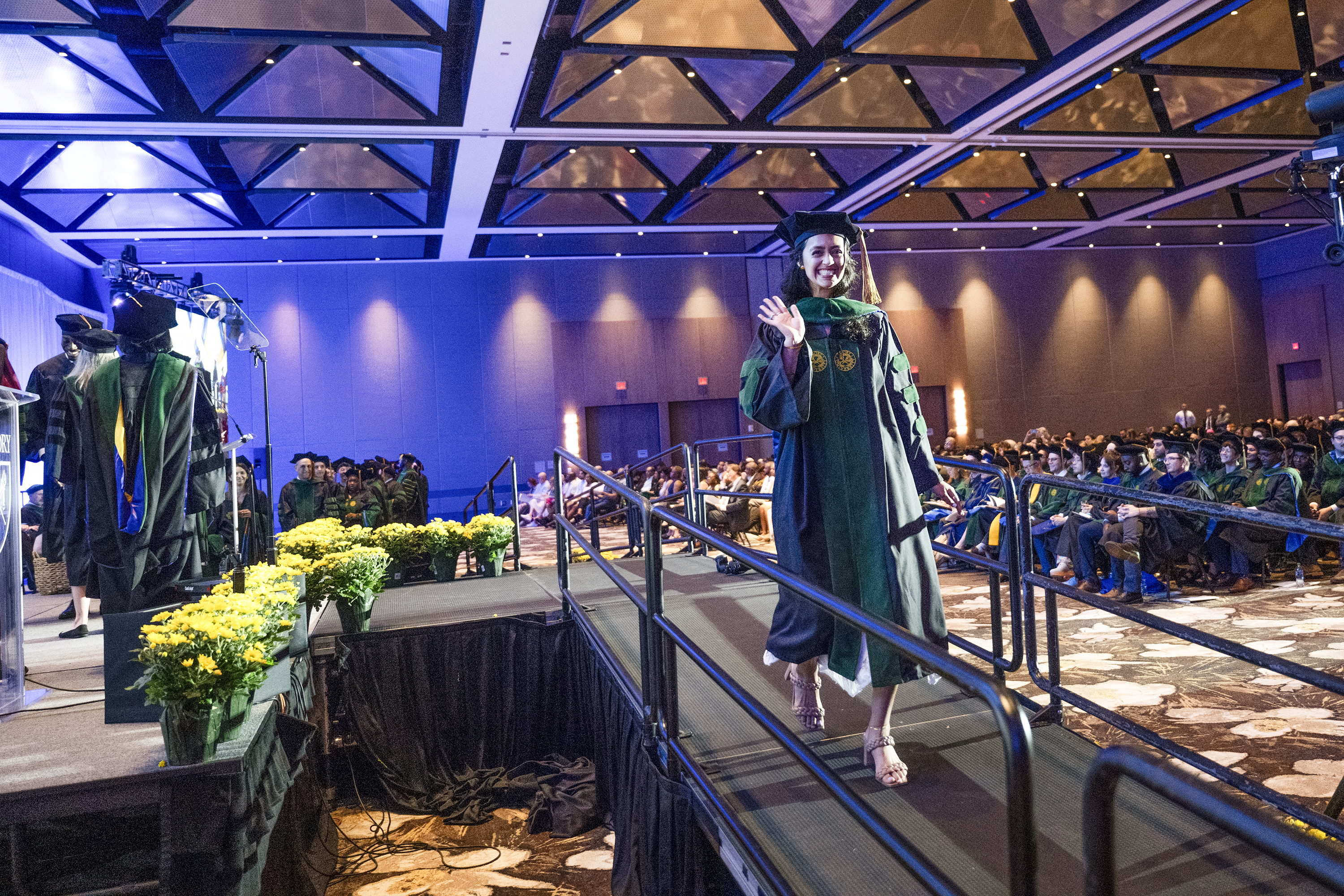 woman walking down a stage ramp at graduation waving
